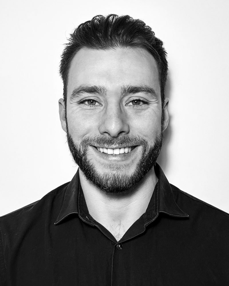 Portrait de Loïc Legrand, souriant, en chemise noire, sur fond clair